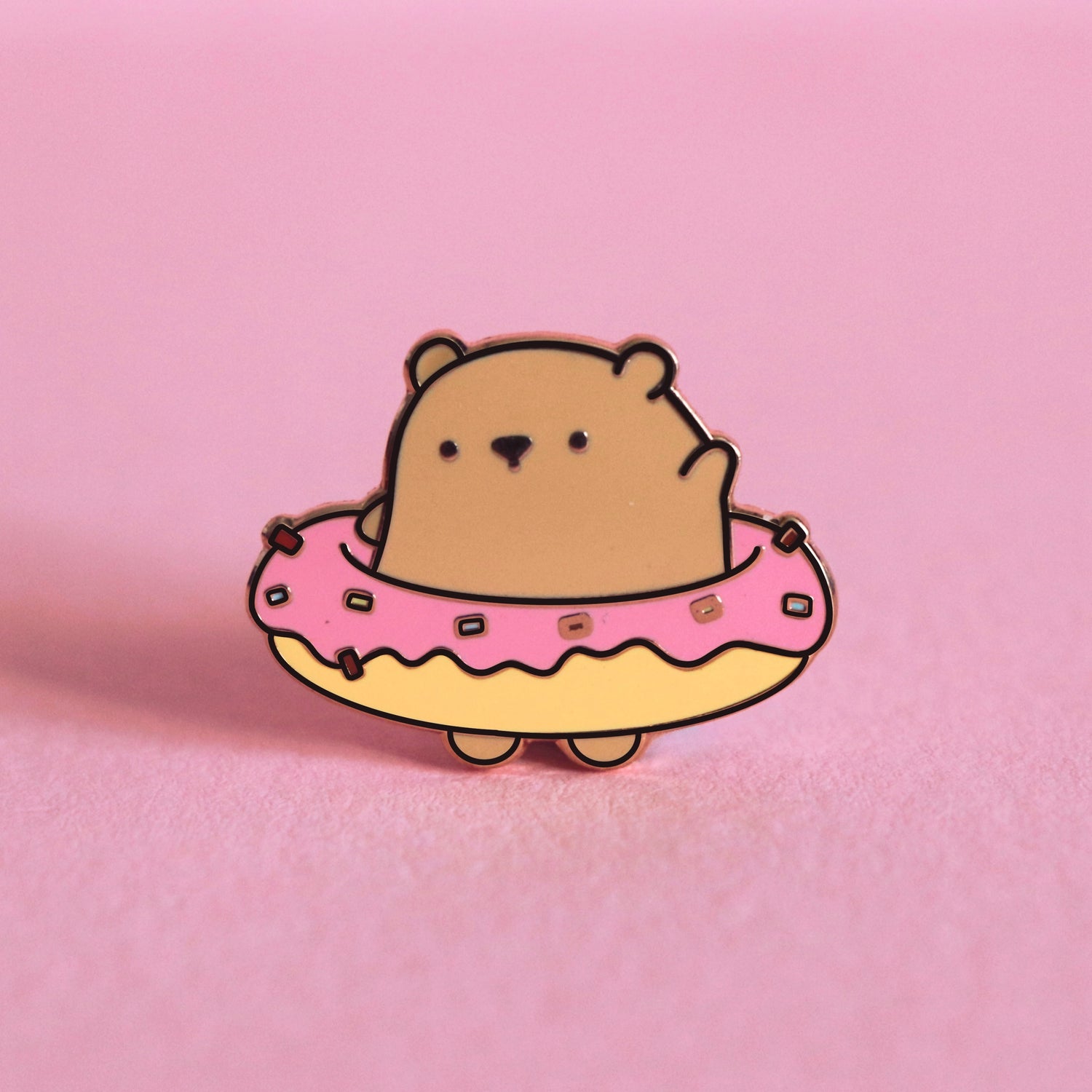 Bear wearing donut enamel pin on pink table