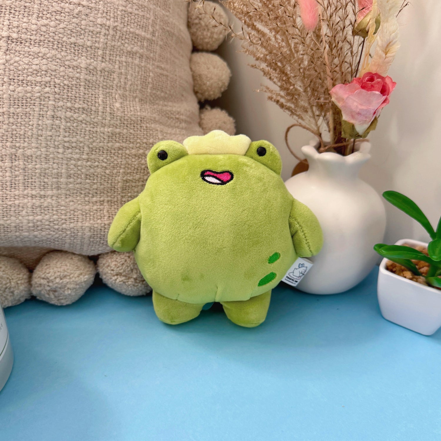 Frog keychain plush with flowers and cushion on blue table