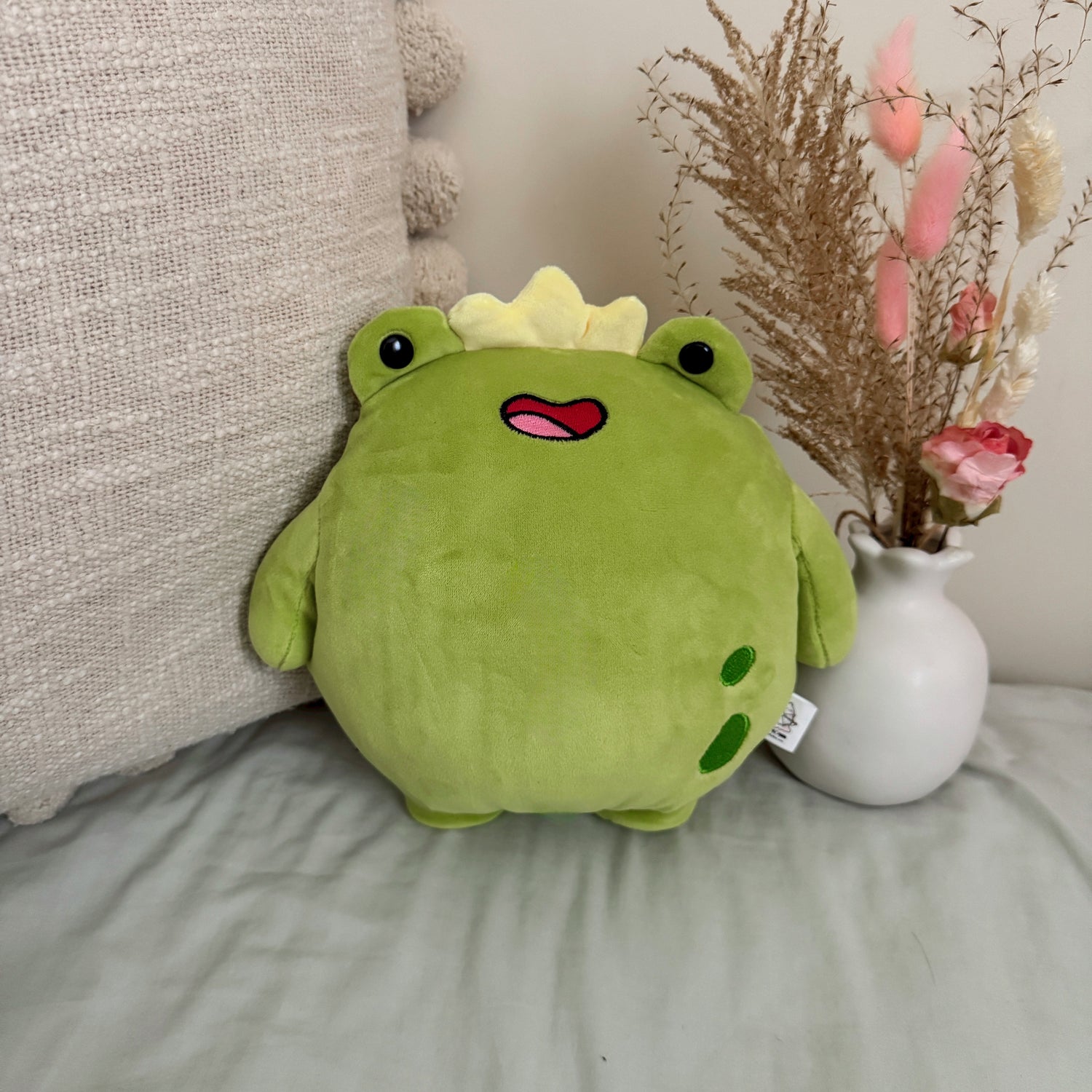 Frog plush toy with flowers and beige cushion