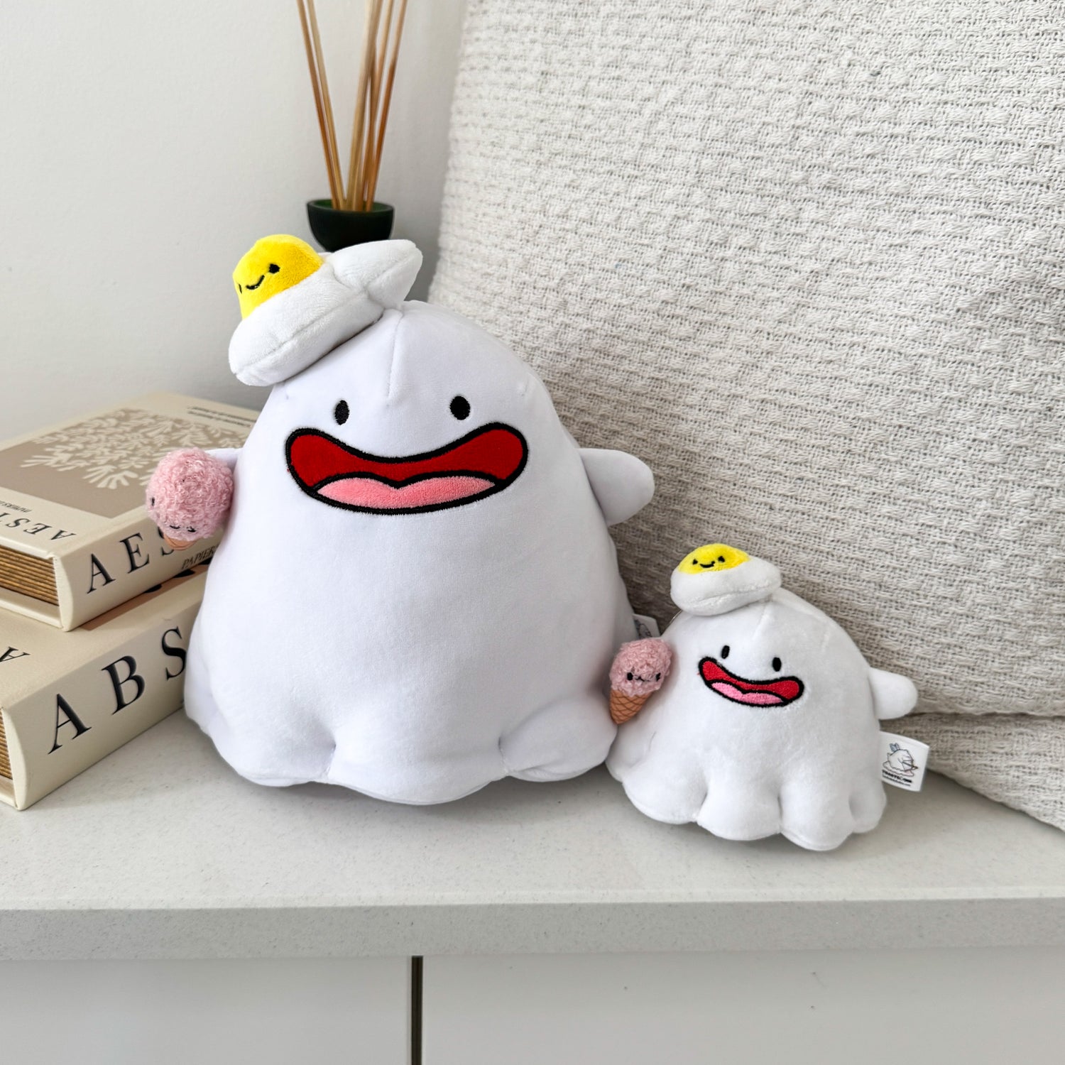 Ghost plush and plush keychain on white table with cushion