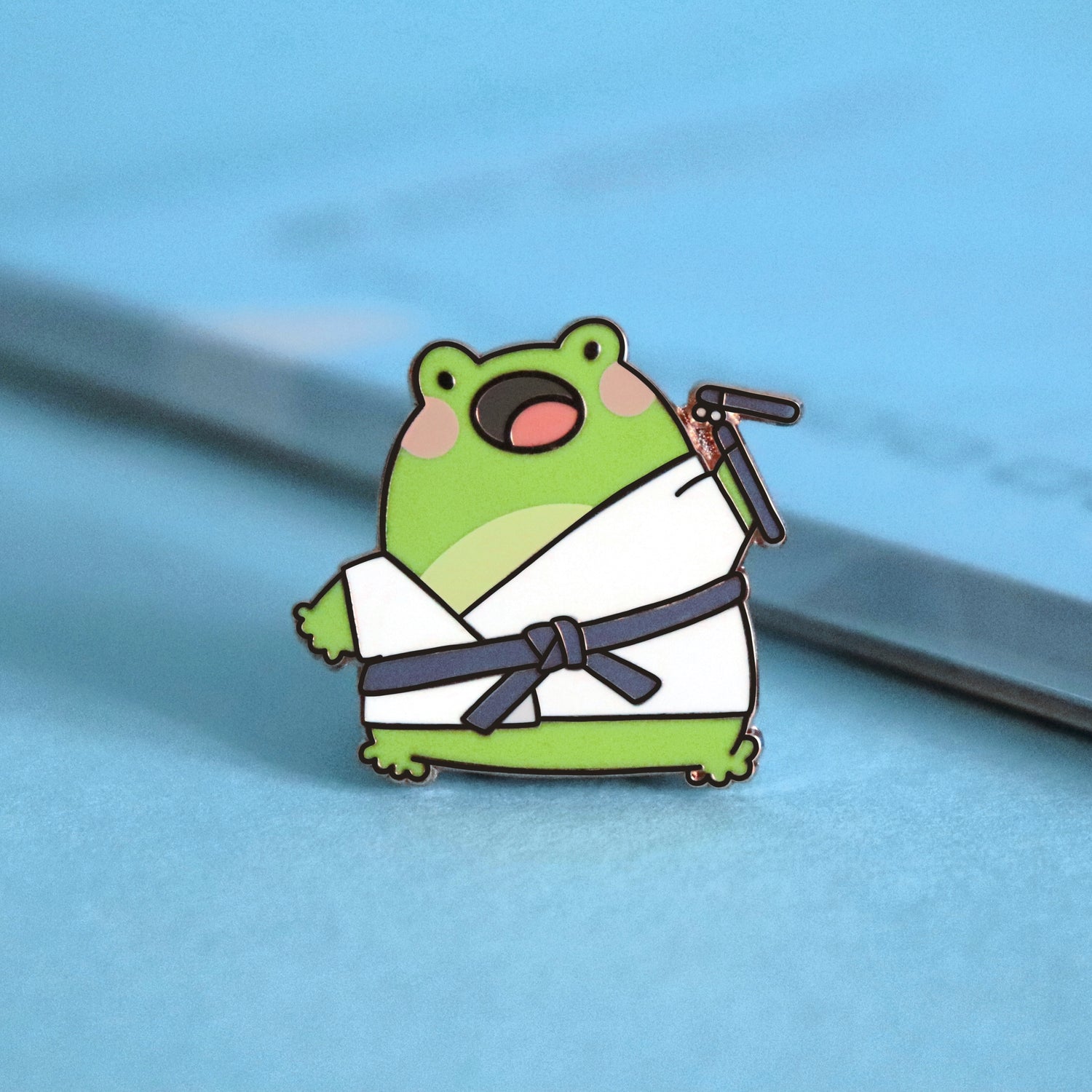 Karate frog enamel pin on blue table with notepad
