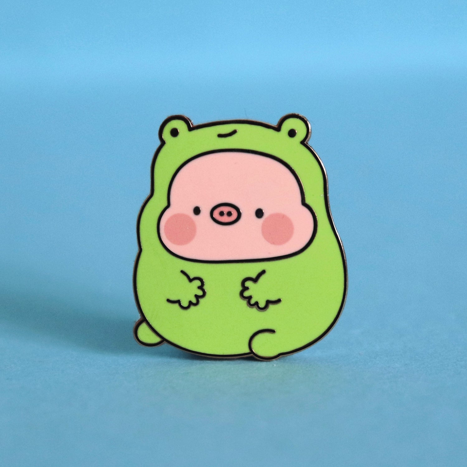 Pig in frog costume enamel pin on blue desk