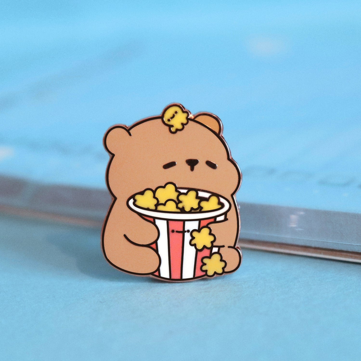 Bear with popcorn enamel pin on blue table