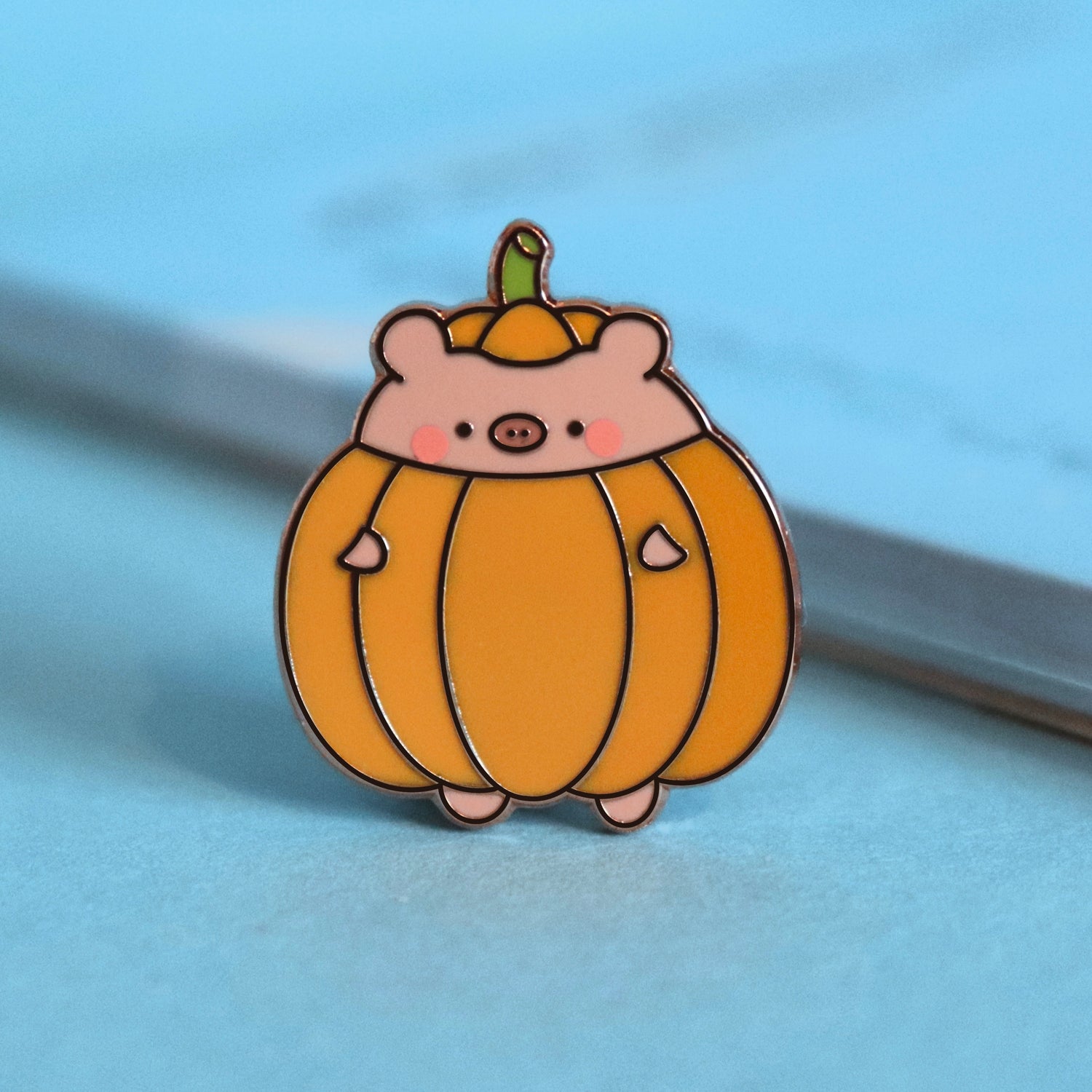 pig dressed as pumpkin enamel pin on blue table with notepad