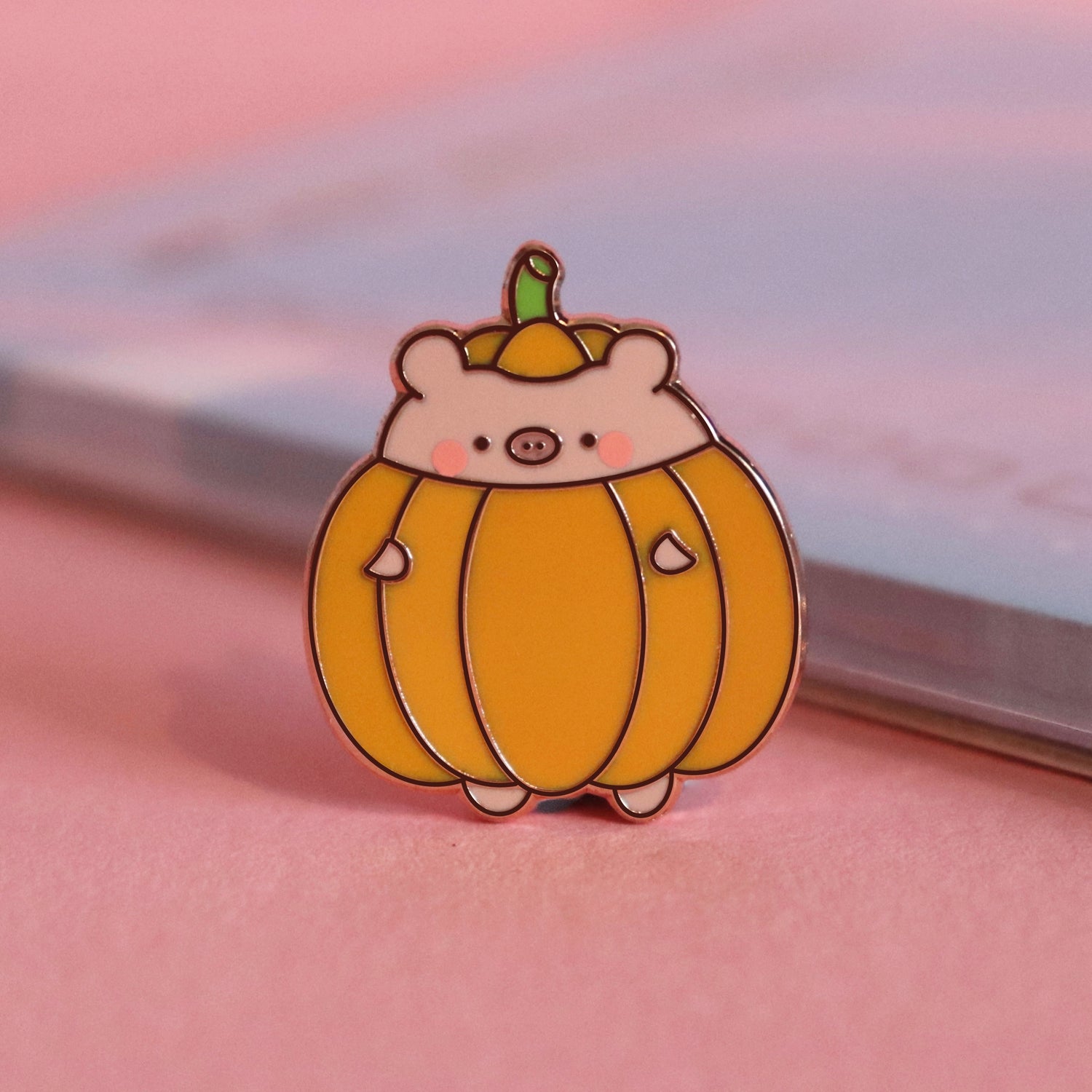 pig dressed as pumpkin enamel pin on pink table with notepad