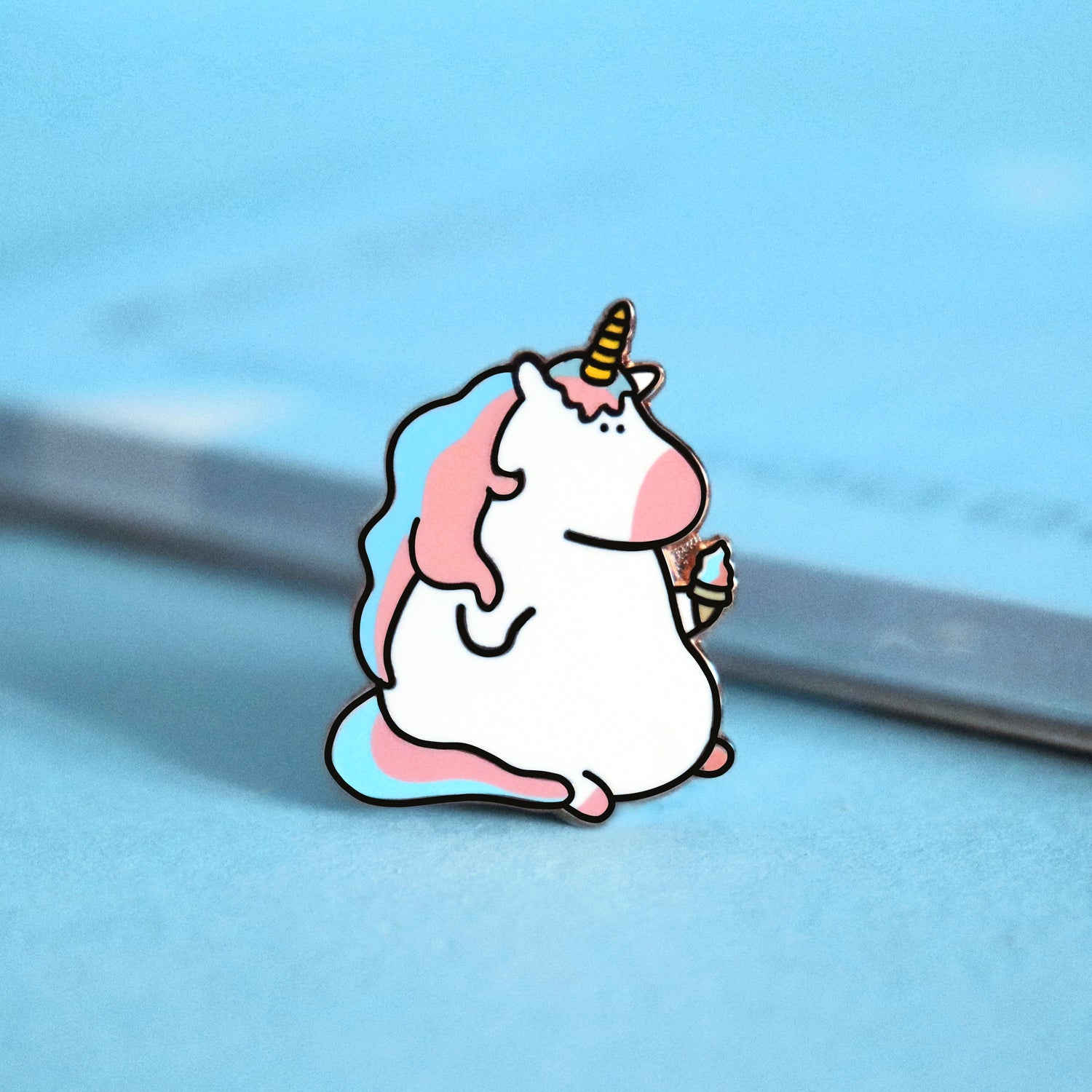 Unicorn enamel pin on blue background with notepad