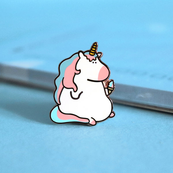 Unicorn enamel pin on blue table with notepad