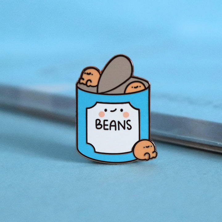 Baked beans enamel pin on blue table with notebook