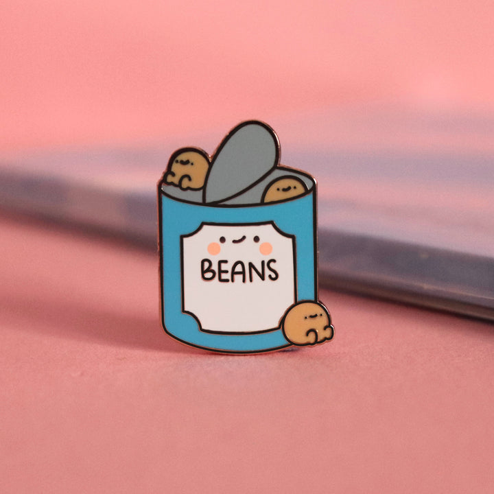 Baked beans enamel pin on pink table with notebook