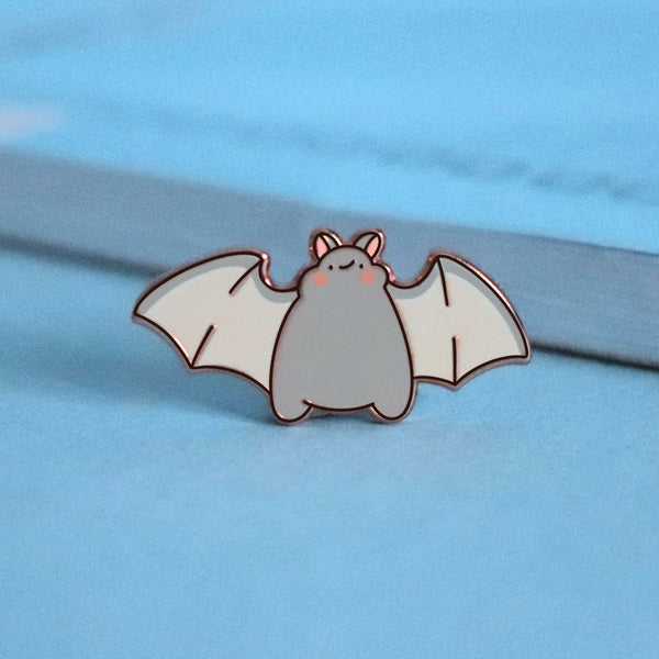 Bat smiling enamel pin on blue table with notepad