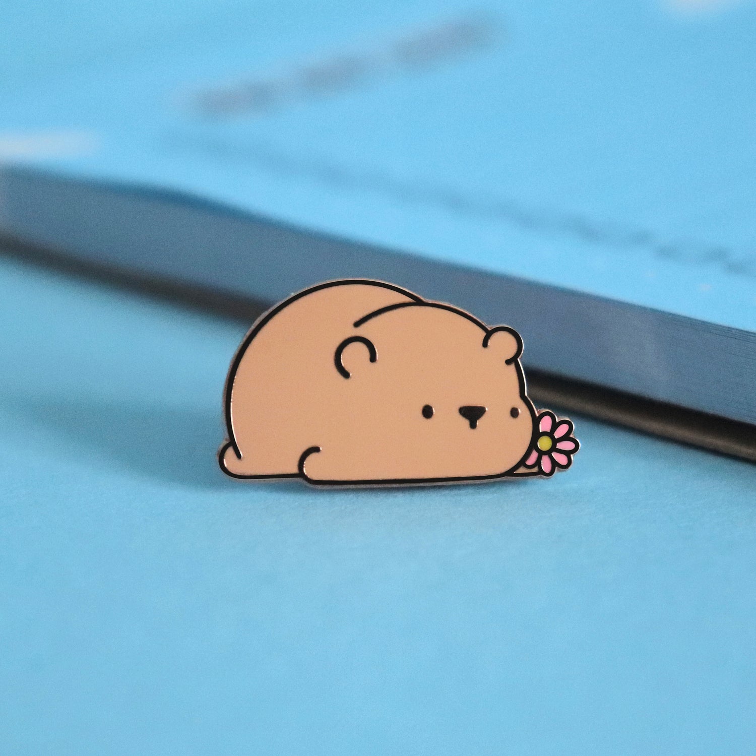 Brown bear enamel pin on blue table with notepad