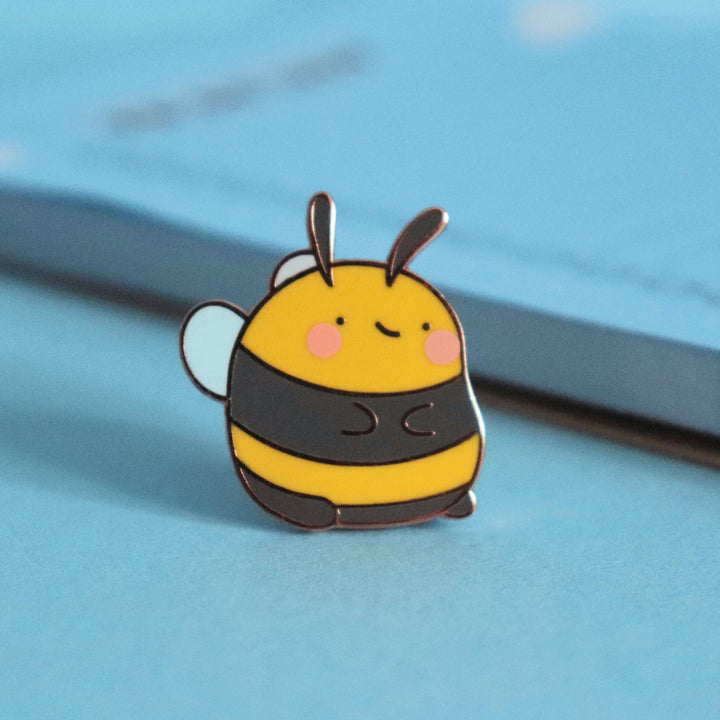 Bee enamel pin on blue table with notepad
