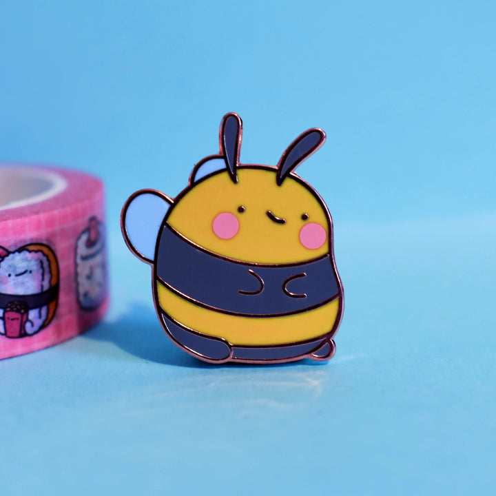 Bee enamel pin on blue table with washi tape