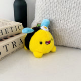Bee plush keychain on beige table with cushion and books