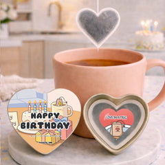 Heart-shaped tea bags with 'Happy Birthday' and 'Love in a Mug' designs next to a pink mug with tea.