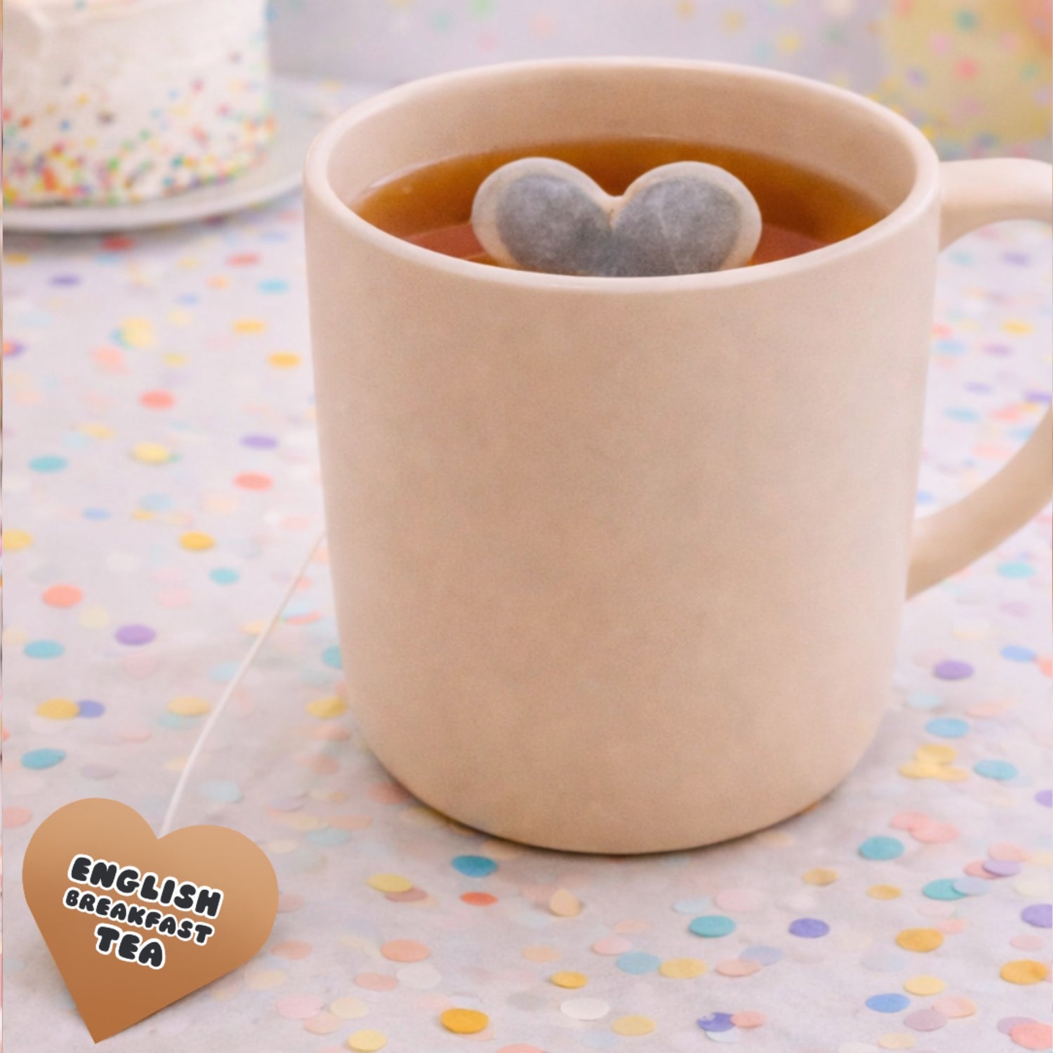 Beige mug with heart-shaped tea bags in a cup of tea on a polka dot tablecloth.