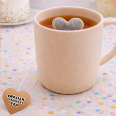 Beige mug with heart-shaped tea bags in a cup of tea on a polka dot tablecloth.
