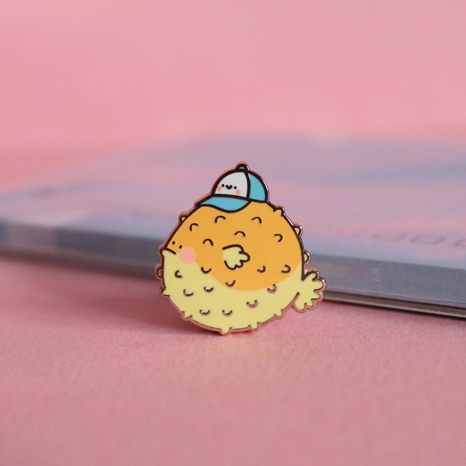 Blowfish enamel pin on pink table and notepad