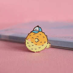 Blowfish enamel pin on pink table and notepad