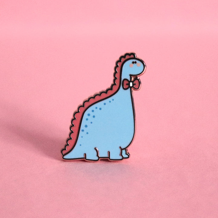 Blue dinosaur with bow tie enamel pin on pink desk