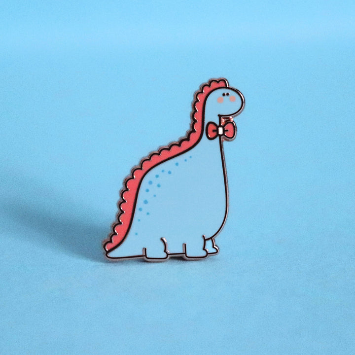 Blue dinosaur with bow tie enamel pin on blue table