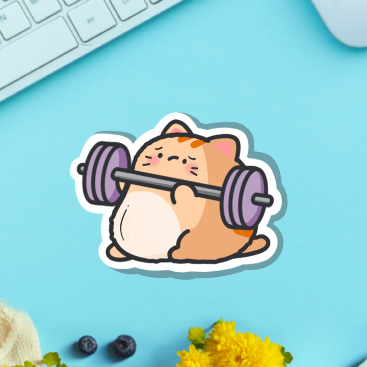 Cat lifting weights vinyl sticker on blue table with keyboard