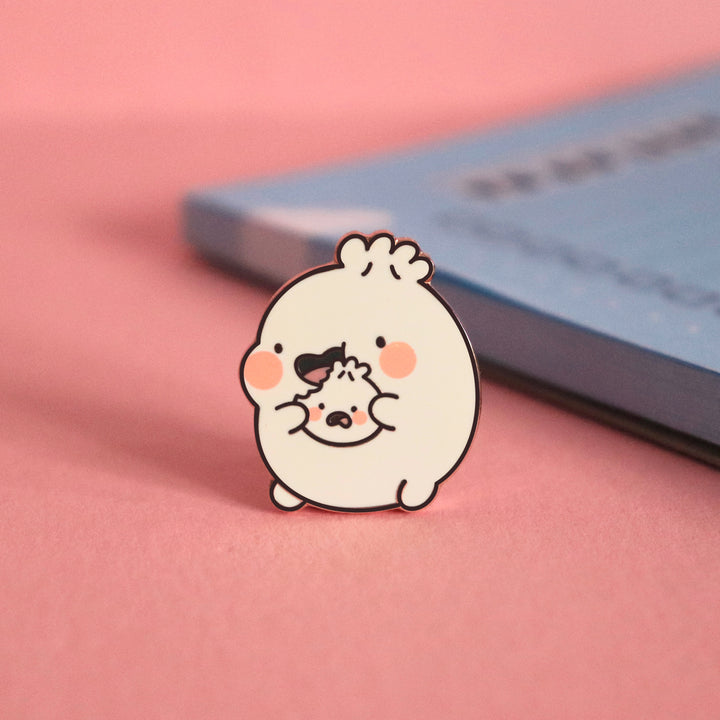 Dumpling eating enamel pin on pink table with notepad