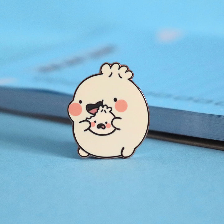 Dumpling eating enamel pin on blue table with notepad