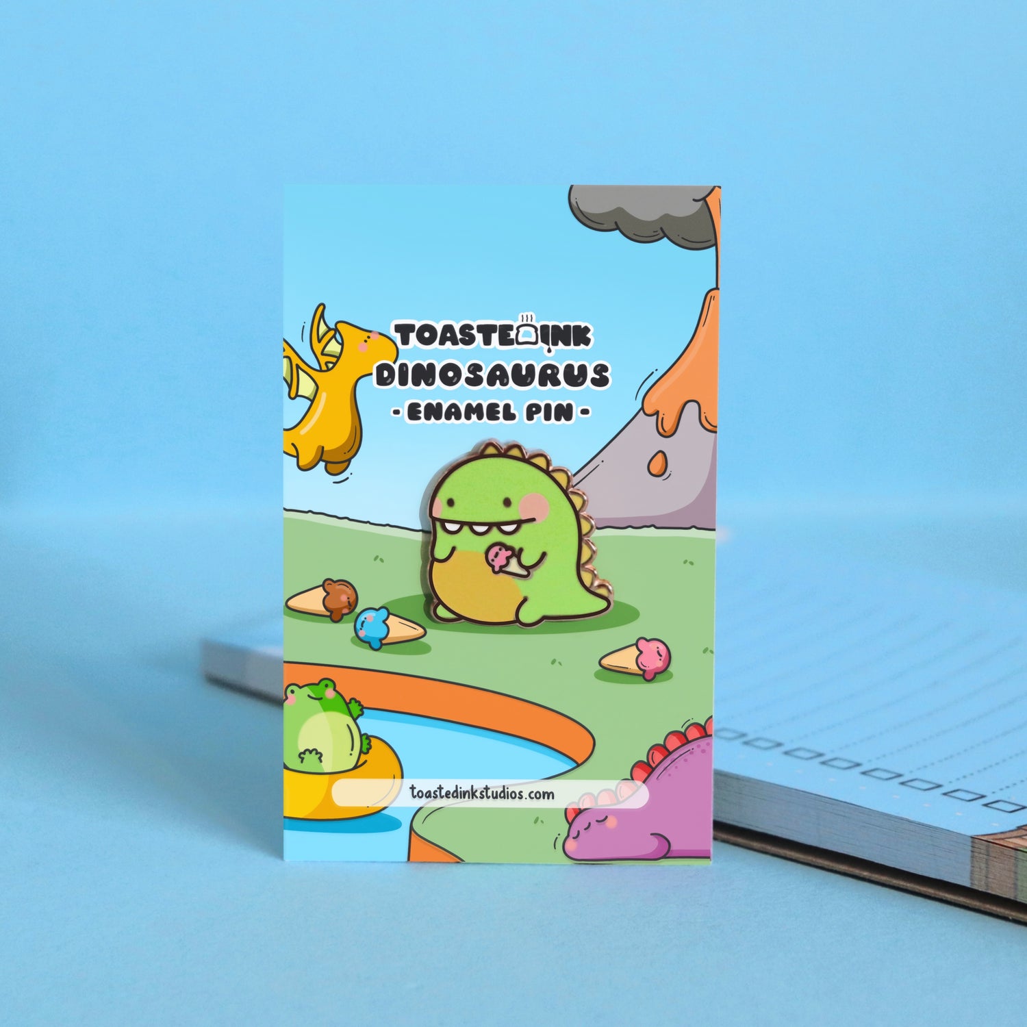 Dinosaur enamel pin on backing card and blue table