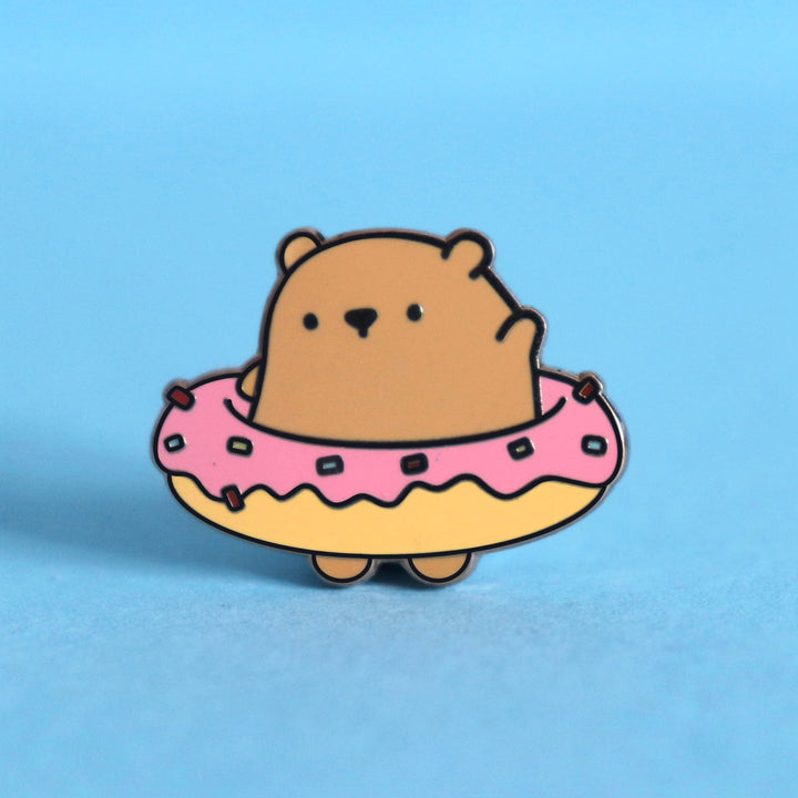 Bear wearing donut enamel pin on blue desk