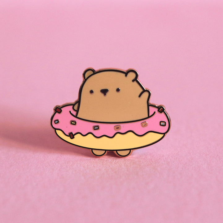 Bear wearing donut enamel pin on pink table