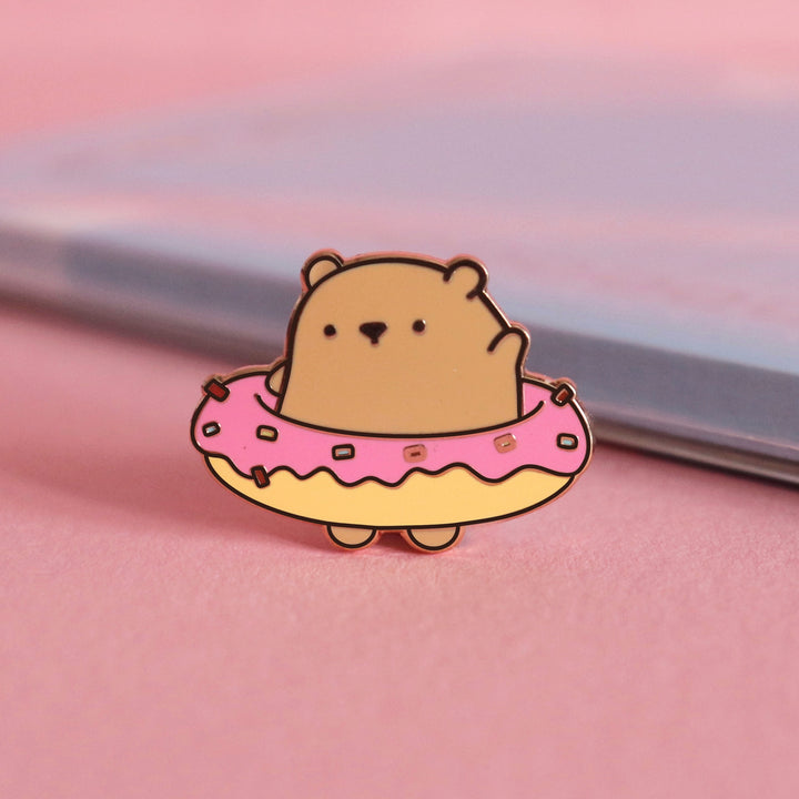 Bear wearing donut enamel pin on pink desk with notepad