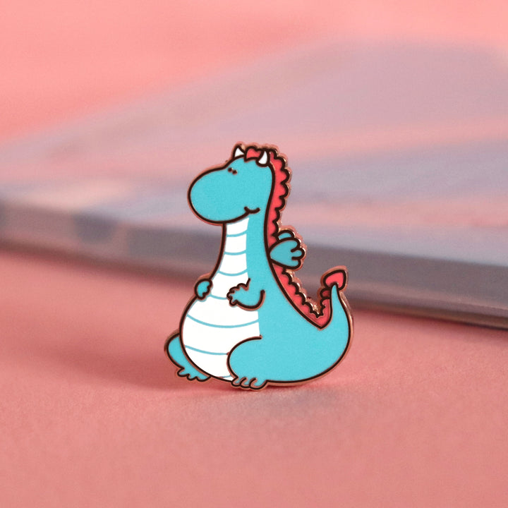 Dragon enamel pin on pink table with notepad