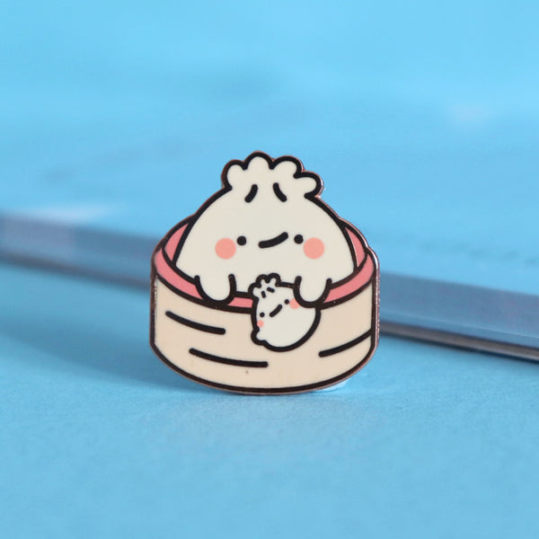 Dumpling enamel pin on blue table with notepad