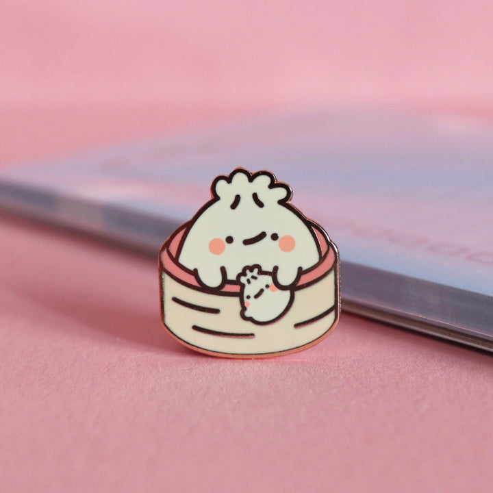 Dumpling enamel pin on pink table with notepad