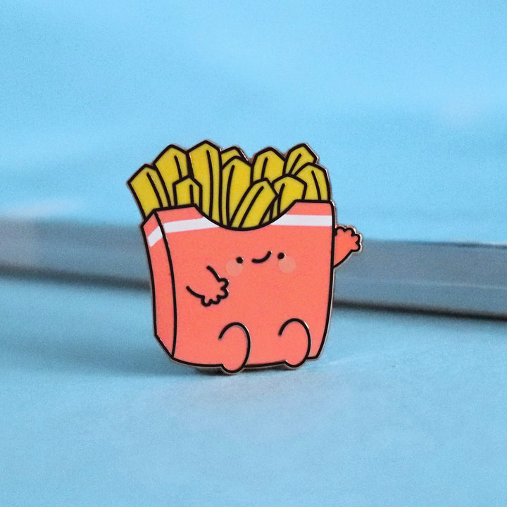 French fries enamel pin on blue table with notepad