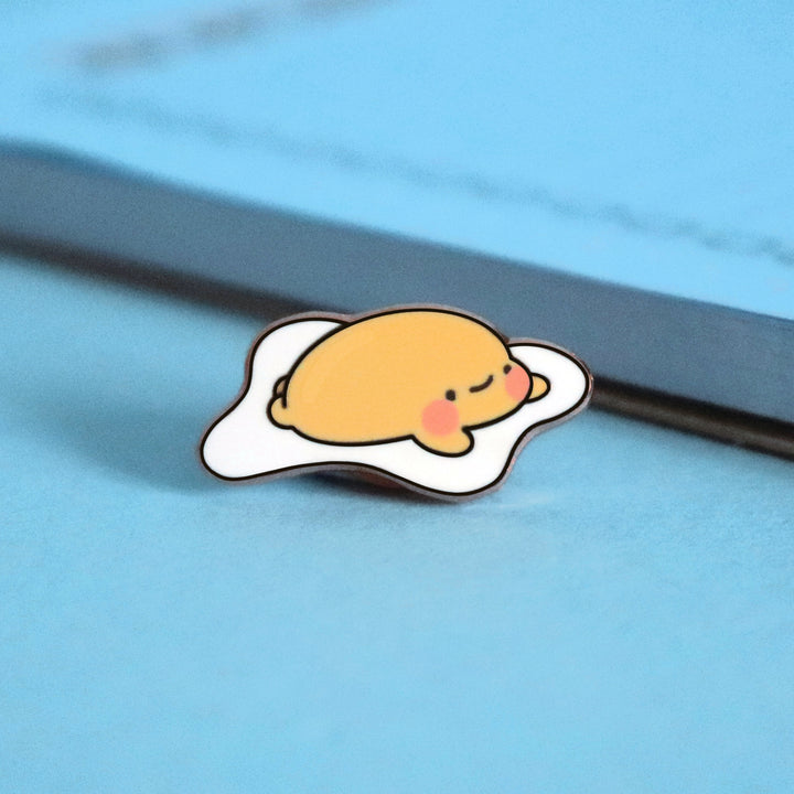 Fried egg enamel pin on blue table with notepad