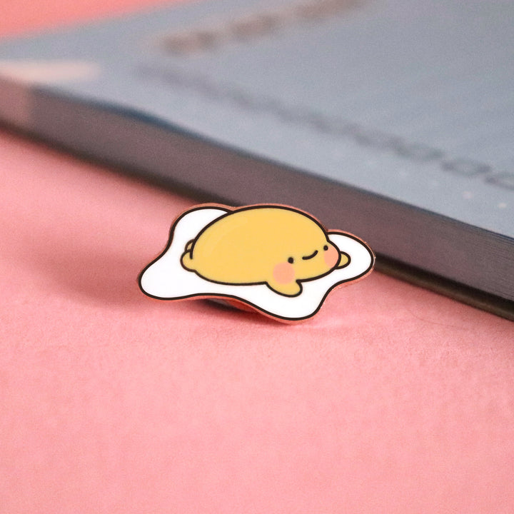 Fried egg enamel pin on pink table with notepad