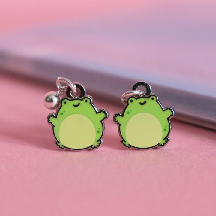 Frog stud earrings on pink desk with notepad