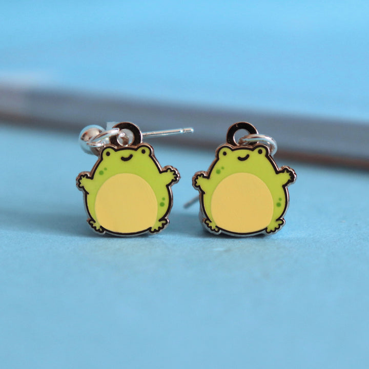 Frog stud earrings on blue table with notepad