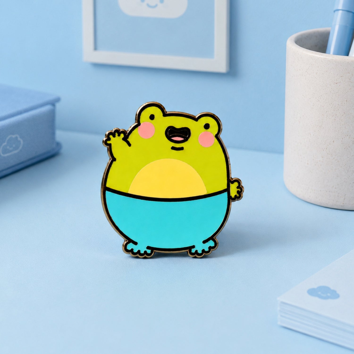 Frog Enamel Pin on blue table with pot of pens