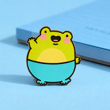 Waving Frog Enamel pin next to blue notepad