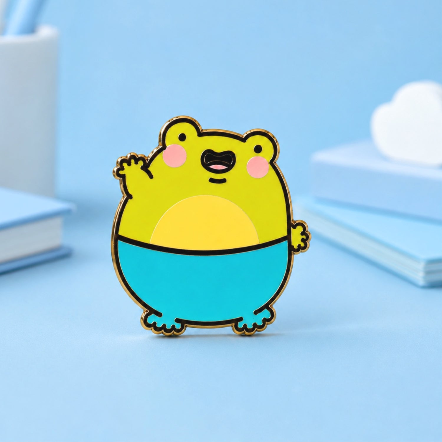 Frog Enamel Pin on blue table with notebooks