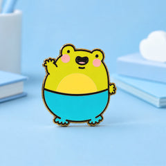Frog Enamel Pin on blue table with notebooks
