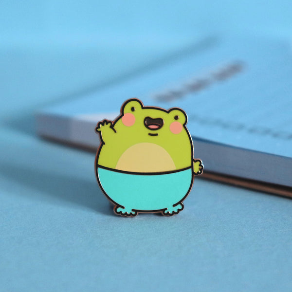 Frog enamel pin on blue background with notepad