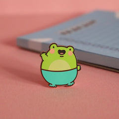Frog enamel pin on pink table with notepad