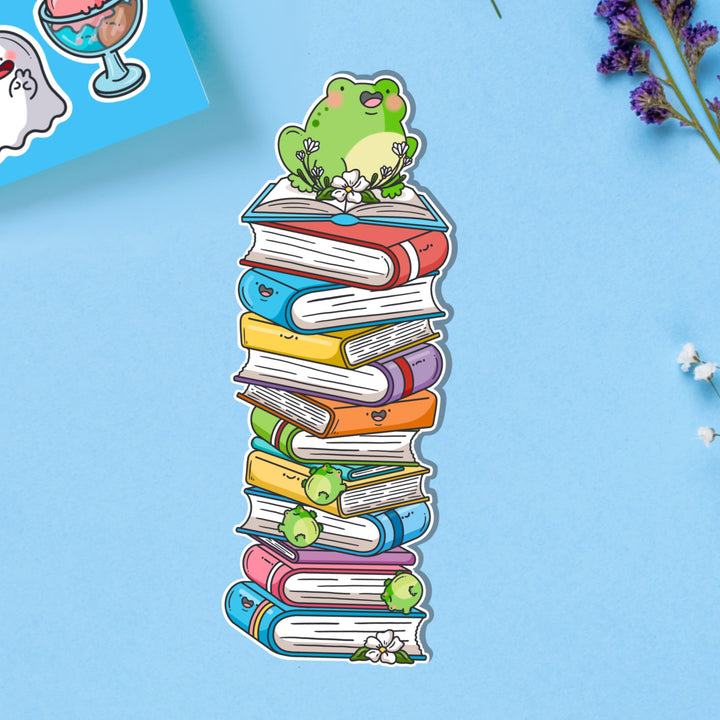 Frog sat on books bookmark on blue table with stickers