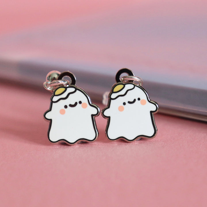 Ghost stud earrings on pink table with notepad