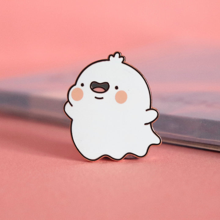 Ghost enamel pin on pink table with notebook
