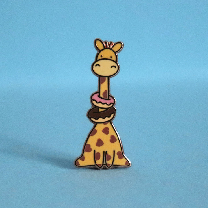 Giraffe with heart prints wearing donuts enamel pin on blue table